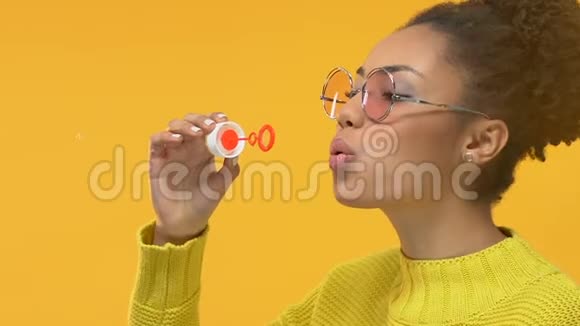快乐的黑人女人在黄色背景上吹肥皂泡青春快乐视频的预览图