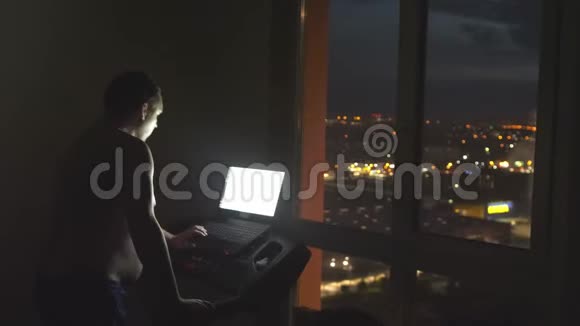 肥胖的年轻人在跑步机上运动晚上用笔记本在全景窗旁工作灯光和灯光视频的预览图