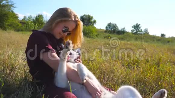 多莉拍了一张太阳镜坐在草地上拥抱着她的哈士奇狗金发美女视频的预览图