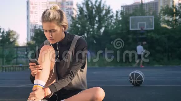 可爱的快乐女篮球运动员戴着耳机打着电话坐在地上男人在玩视频的预览图