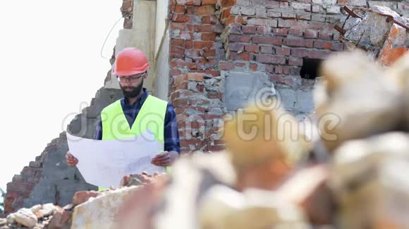 认真的建设者分析图纸有胡子的建筑工程师戴着头盔在被摧毁的建筑背景上视频的预览图