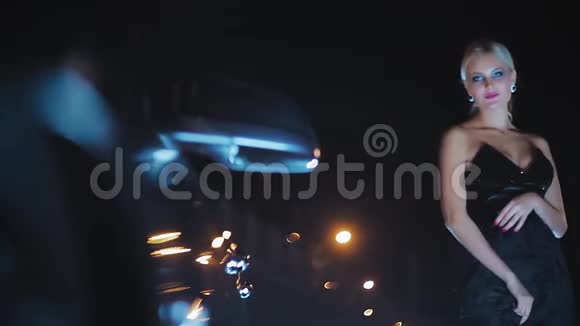 一个漂亮的金发美女晚上在一辆车旁边摆着黑色的裙子视频的预览图