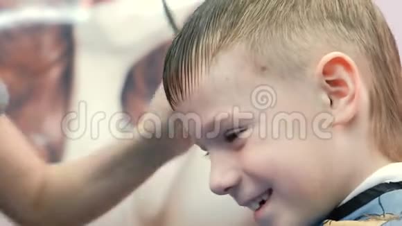 特写理发师他的手梳和剪刘海金发的短男孩他的头发用剪刀视频的预览图