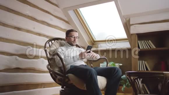 戴眼镜的男人在椅子上的智能手机上自拍视频的预览图