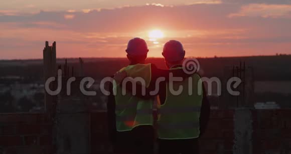 两个朋友和伙伴在建筑屋顶的建筑工地上互相拥抱看着令人惊叹的天空景色视频的预览图