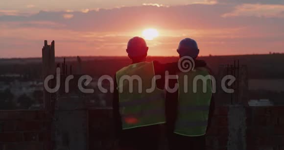 建筑工地两个伙伴看着令人惊叹的城市景色和日落像朋友一样抱在一起视频的预览图