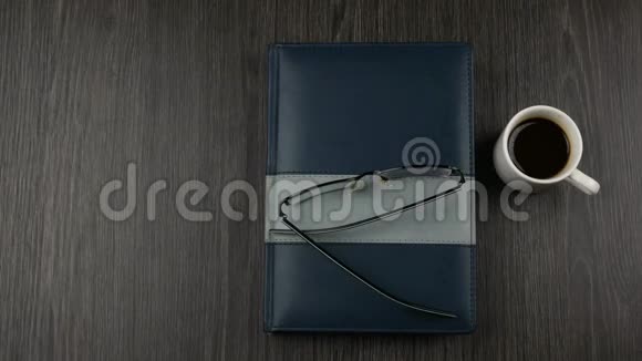 灰色覆盖记事本和一杯咖啡在黑暗的木制背景打开书写记事本视频的预览图