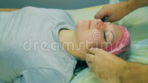 化妆师的男人的手从躺在沙发上的女人的头上移开一顶化妆帽视频的预览图