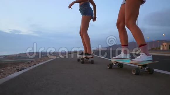 两个女孩滑板车骑在一个木板上的斜坡与天空从山上慢动作稳定视频的预览图