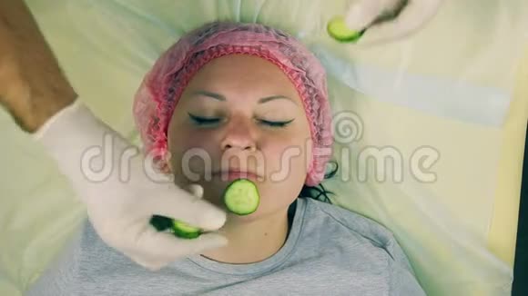 戴着手套的化妆师的男人的手放在女人脸上的黄瓜片上视频的预览图