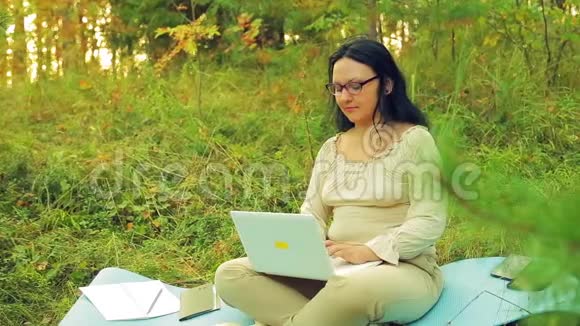 一个带眼镜的黑发女人戴着眼镜在林中空地上用笔记本电脑工作视频的预览图