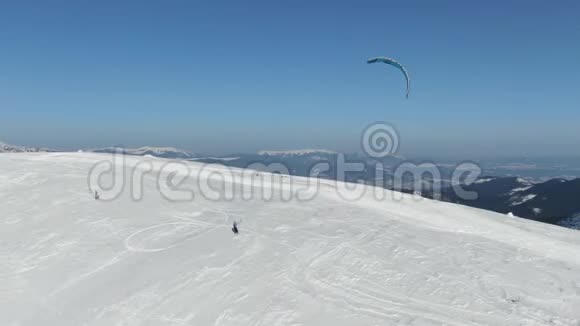 在阳光明媚的一天使用滑翔机沿着雪坡滑雪的速度滑行者空中射击视频的预览图