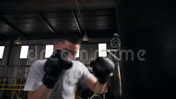 特写一个男拳击手在健身房锻炼的镜头用拳击袋训练过程拳击手戴黑色拳击手套视频的预览图