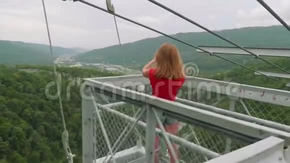 镜头接近年轻的金发女子自拍在高悬桥上的青山谷视频的预览图