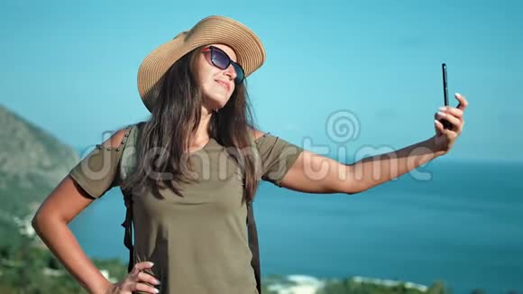 戴帽子戴墨镜戴智能手机拍照的微笑女旅行者肖像视频的预览图