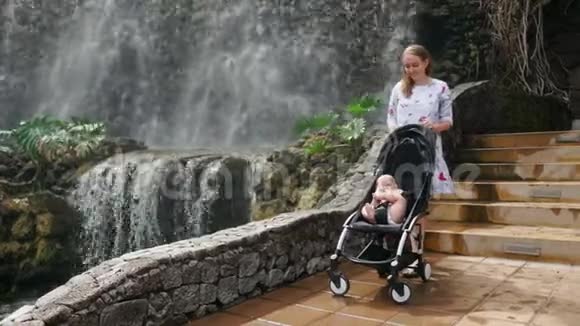 在一次家庭旅行中坐在轮椅上的婴儿笑着看着瀑布妈妈带着孩子散步视频的预览图