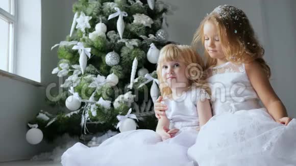 小女孩抱着妹妹微笑着在背景圣诞树上戴着装饰物的假雪头发视频的预览图