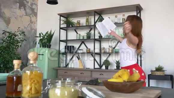 迷人的美女有姜发会读烹饪书在现代厨房跳舞在家玩得很开心视频的预览图