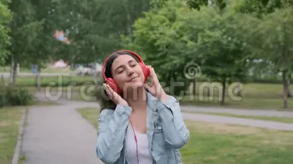 美丽欢快的女孩带着耳机在公园里跳舞视频的预览图