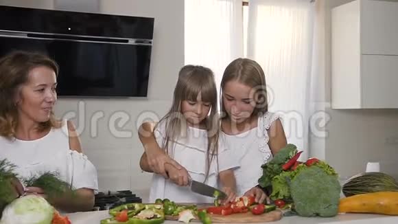 两个姐姐和妈妈穿着白色连衣裙一起在厨房里做健康的蔬菜沙拉二视频的预览图