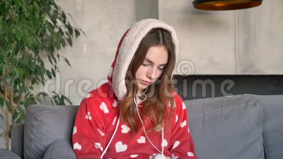 一位留着姜发的美女戴着头罩通过耳机听音乐坐在客厅的沙发上视频的预览图