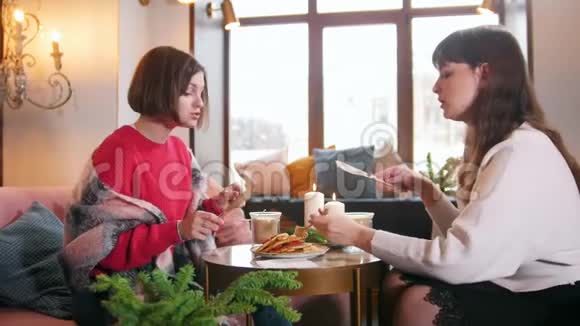 两个年轻的女人坐在咖啡馆里边吃煎饼边说话伟大的内部视频的预览图