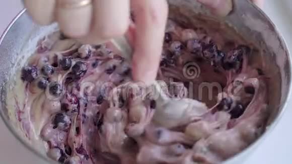 女用勺子在不锈钢碗里准备蓝莓派的面团视频的预览图