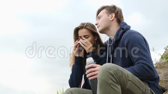 一个男人和一个女孩坐在河岸上喝热水瓶里的茶视频的预览图