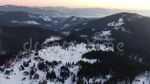 华丽的空中拍摄山上覆盖着树木和雪前面有一个小村庄4k视频的预览图
