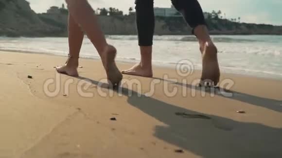男人和女人的腿沿着海滩走得很近夫妻俩光着脚在沙滩上散步年轻快乐的休闲视频的预览图