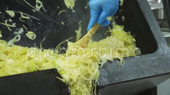 特写镜头一个戴着手套的厨师从一个大的工业煎锅里倒出许多炸洋葱来烤视频的预览图