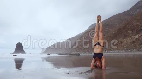在海洋边一个女人在瑜伽倒立和冥想健康的生活方式站在沙滩上平衡你的头视频的预览图