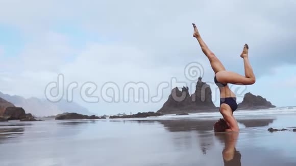 运动女孩站在她的头上在海洋上移动她的腿在空中缠绕拉伸视频的预览图