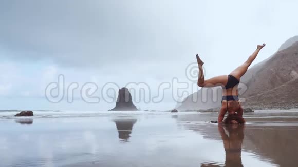 运动女孩站在她的头上在海洋上移动她的腿在空中缠绕拉伸视频的预览图