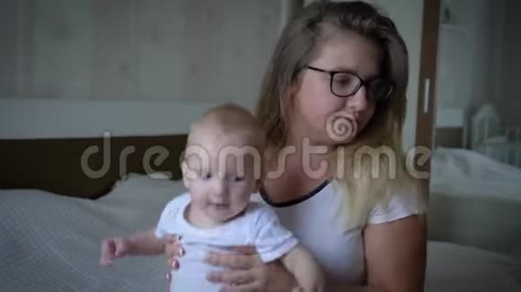压力很大戴眼镜的紧张的妈妈常常把坐在床上的婴儿举起手来视频的预览图