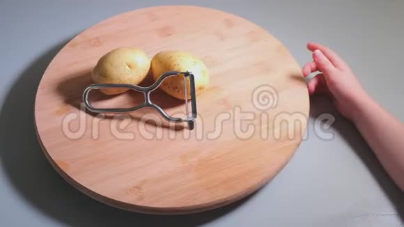 小女孩的手在木桌上用削皮机剥土豆皮视频的预览图
