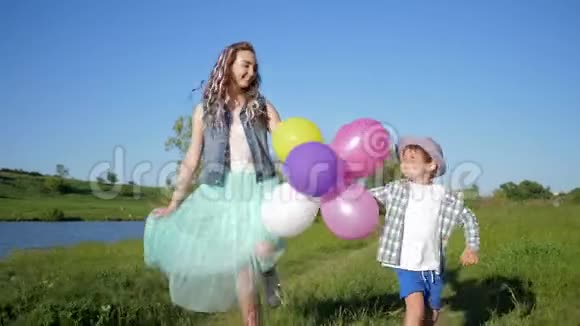 微笑的孩子们带着彩色的球跳跃的乐趣牵着手在湖边的大自然视频的预览图