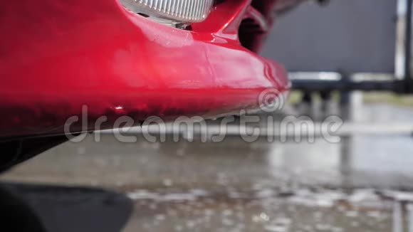 水和泡沫洗涤剂从一辆红色洗过的汽车在自助洗车中排出视频的预览图