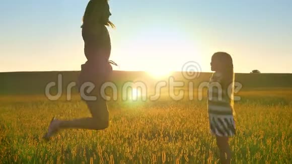 年轻的母亲和小女儿一头金发在麦田中央跳跃微笑着美丽视频的预览图