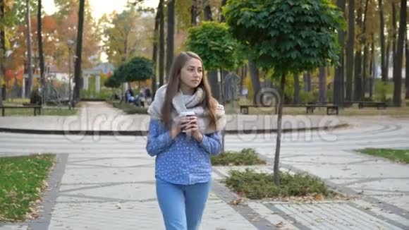 在秋天公园喝热茶或咖啡的女人的脸上她戴着针织围巾女孩喝咖啡视频的预览图