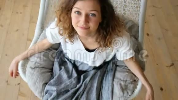 年轻的欧洲女孩穿着亚麻衣服在一间阁楼的公寓里吊床上荡秋直视着镜头视频的预览图
