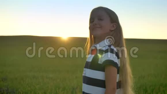 美丽的金发小女孩站在麦田里对着镜头微笑夕阳下美丽的景色视频的预览图