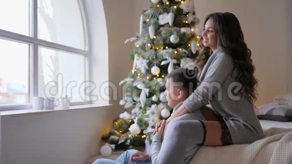 庆祝气氛女孩坐在沙发上拥抱她的男朋友看着窗外靠近圣诞树视频的预览图