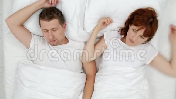 在喧闹的夜晚打鼾的男人哽咽着大声叫醒他的妻子她用枕头闭上耳朵上文视视频的预览图