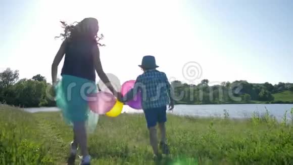 快乐的孩子们手拿彩色气球在绿色的草坪上漫步视频的预览图