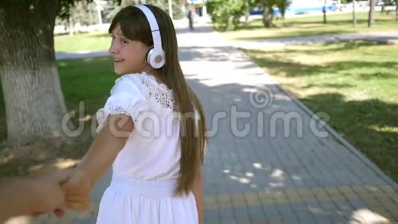 戴着耳机的女孩微笑着牵着心爱的男人的手在公园里度过了一个春天的日子有爱心的团队合作视频的预览图