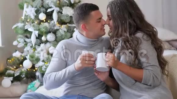 情侣们微笑着早上在装饰好的圣诞树上的家沙发上喝咖啡视频的预览图
