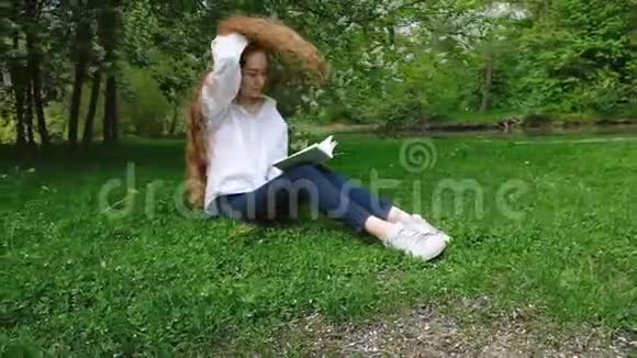 欧洲女孩把长长的卷发扔回去在大自然中读一本书相机运动女青年休息视频的预览图