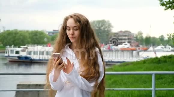 美丽的年轻的欧洲女孩打电话在水边的河边通过电话交谈动作缓慢女人很长视频的预览图
