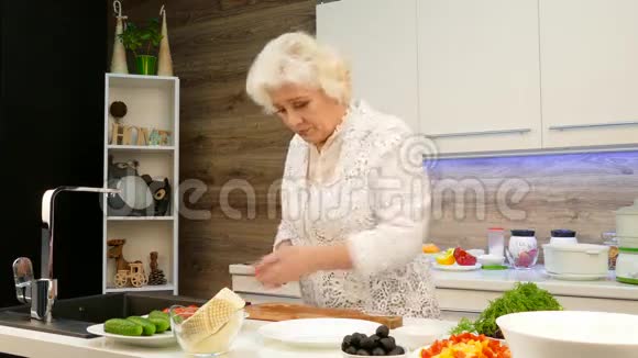 成熟的白发女人在厨房里切樱桃番茄做沙拉视频的预览图